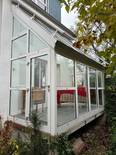 Gartenhaus mit großflächigen Fenstern und rotem Tisch im Inneren.