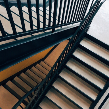Schwarz-weiße Treppe mit Metallgeländer, von oben betrachtet.