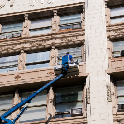 Arbeiter reinigt Fenster eines historischen Gebäudes mit einem Hubarbeitsbühne.