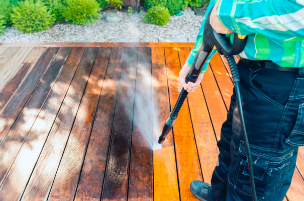 Person reinigt mit Hochdruckreiniger eine Holzterrasse.