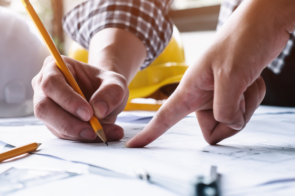 Hände, die auf Baupläne zeigen und mit einem Bleistift arbeiten.