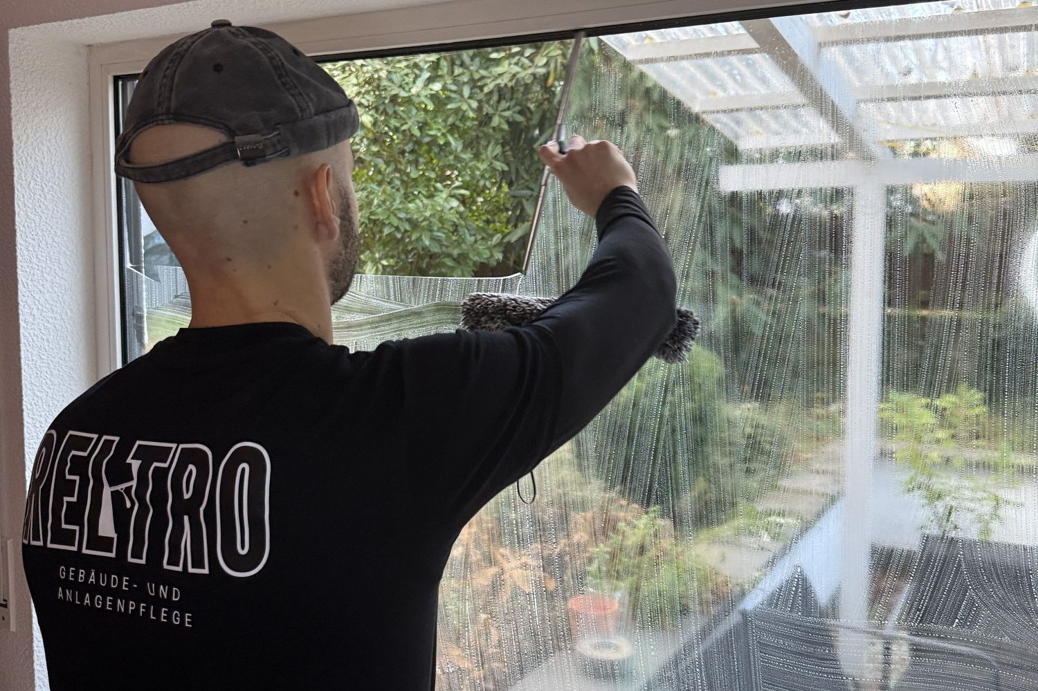 Ein Mann reinigt ein Fenster mit einem Einwascher und Abzieher unter blauem Himmel.