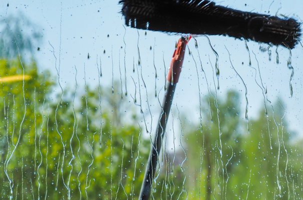 Wassertropfen fließen an einer Fensterscheibe mit einem Fensterwischer herab.