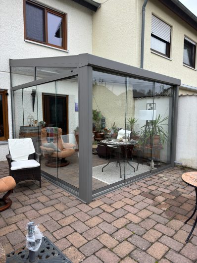 Gartenpavillon mit Glaswänden und gemütlichen Sitzgelegenheiten.
